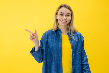 Astonished girl pointing to side empty place on yellow background and smile expressing amazement,...