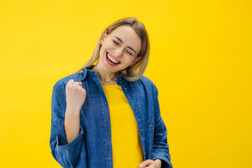 I did it! Portrait of closed eyes raised fist up woman in casual wear isolated on yellow background...