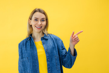 Beautiful happy blond woman pointing with forefinger over empty isolated yellow background.