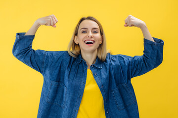 healthy young woman flexing both arms muscles on yellow background