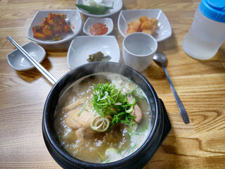 A bowl of soup with green onions on top sits on a wooden table. The table is set with various bowls, cups, and spoons, and there is a bottle of water nearby. Concept of comfort and warmth