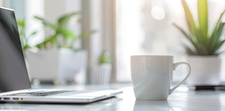 Minimalist white office desk with laptop and coffee mug on blurred background