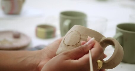 Close-up of the hands of a young African American woman painting a sun on a clay mug at a pottery master class. Creative workshops for adults.