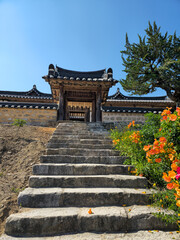 Fototapeta premium A stone staircase leads up to a building with a large door. The door is open and the stairs are empty. The building is surrounded by a garden with orange flowers