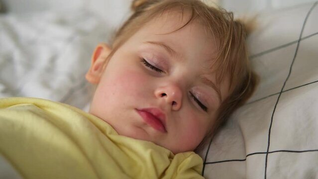 Peaceful adorable baby sleeping on a bed at home. Slumbering little child. Two years old girl sleeps peaceful at domestic room interior background. Serene dream. Cute face close up. Deep kid slumber