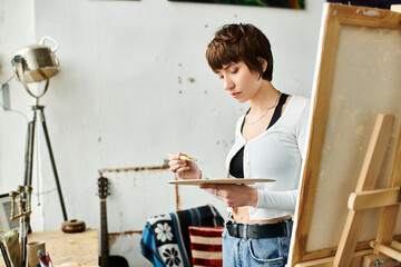 A woman paints at an easel in a studio.