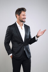 Handsome businessman in black suit smiling, showing and looking with his hand at something
