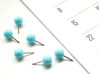A group of unstuck blue push pins next to a monthly paper calendar for marking events or meetings
