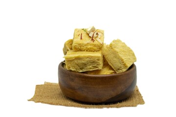 Soan Papdi or Shompapri Garnished with Cashew Nut, Pistachio, Almond and Saffron in Wooden Bowl with Burlap Fabric Isolate on White Background with Copy Space, Also Known as Patisa or Shonpapdi