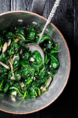 Stewed spinach in copper pan with nuts, butter and garlic close up. Healthy vegan food. Top view