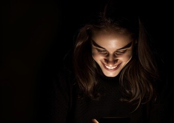 A young woman smiles as she looks at her cell phone, which has a black background, Happy woman using cell phone