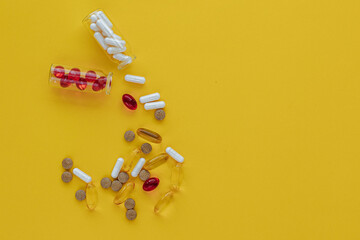 Capsules spill out of small glass bottles on a yellow background
