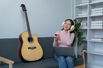 weekend day asian girl is sitting on couch blowing off steam by singing playing guitar at home....