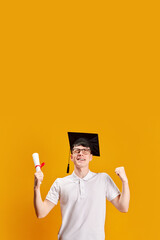Graduation Day Triumph. Happy young man in graduation cap, holing diploma, celebrating against...