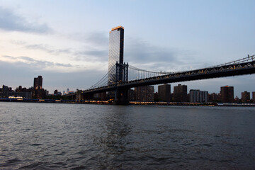 Naklejka premium ManhattanA bridge spans a river in the city of New York. The bridge is lit up at night, creating a beautiful and serene atmosphere.