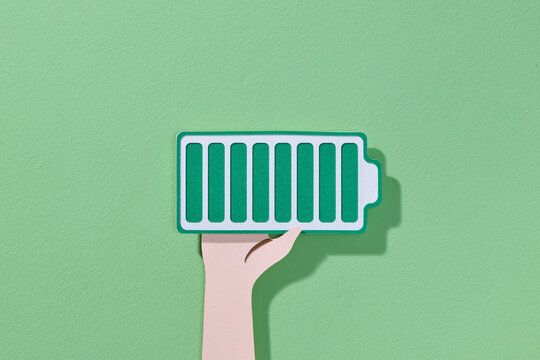 hand holding a paper-cut icon of a battery with full charge level