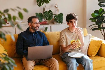 Father and son sitting together on cozy yellow sofa at home