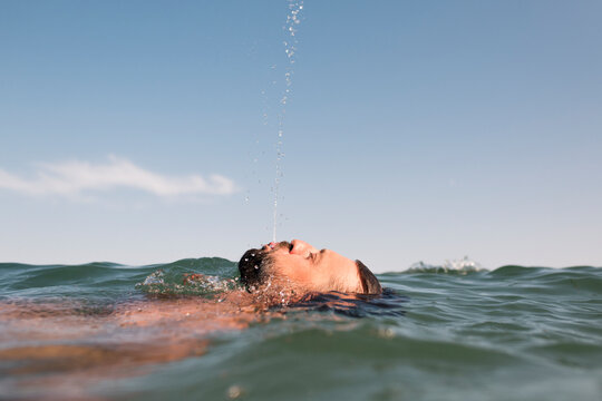Funny floating man spitting water in the sea