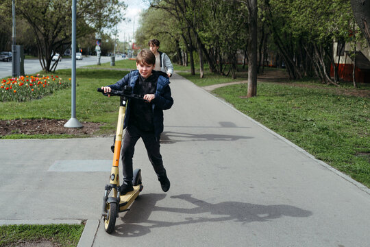 Young Boy Riding Scooter Down Sidewalk
