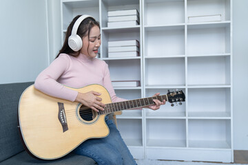 weekend day asian girl is sitting on couch blowing off steam by singing playing guitar at home....