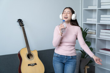 Young singer fun woman wear casual clothes stand near sofa couch using laptop listen music in headphones playing guitar sing song record voice stay home on weekend