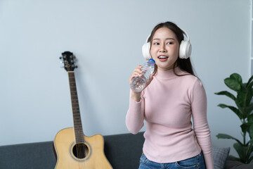 weekend day asian girl is sitting on couch blowing off steam by singing playing guitar at home....