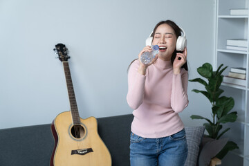 weekend day asian girl is sitting on couch blowing off steam by singing playing guitar at home....