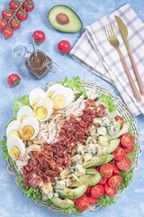 Cobb salad with greens, tomato, avocado, blue cheese, bacon, chicken and eggs, vertical top view