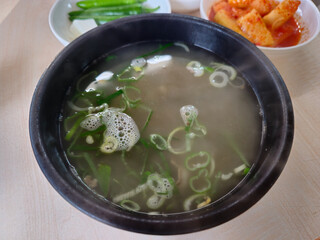 A bowl of soup with green vegetables and a spoon in it. The soup is steaming and has a light green color