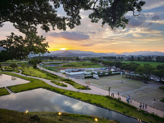 A beautiful sunset over a city with a large park in the background. The park is filled with people enjoying the view and the peaceful atmosphere