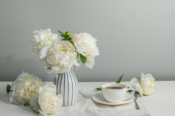 Morning cup of coffee and white peonies in a vase on the table. Summer mood. Copy space.