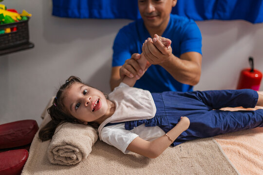 Physiotherapist checking arm of kid lying on bed in clinic