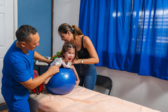 Physiotherapist and mother helping girl put on ball in clinic