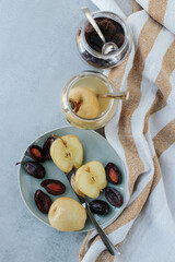 Glass jars with fermented apples and plums stand on a light background. next to it is a plate with a cut fermented apple and plums and a fork.