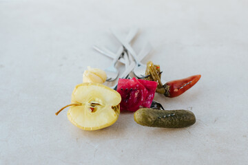 on a light stone background lie forks with impaled 
fermented vegetables: pepper, garlic, cucumber, apple and cabbage.