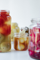Glass jars of different sizes with fermented vegetables stand on a light background. 