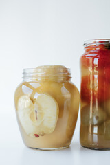 Glass jars of different sizes with fermented vegetables stand on a light background. 