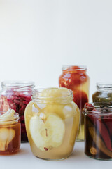 Glass jars of different sizes with fermented vegetables stand on a light background. 