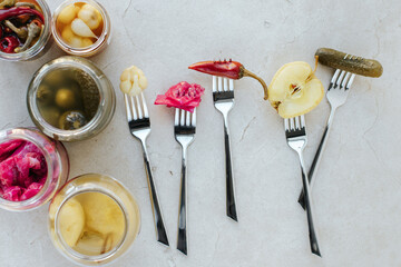 On a light stone background, there are jars with fermented vegetables on the side and next to them...