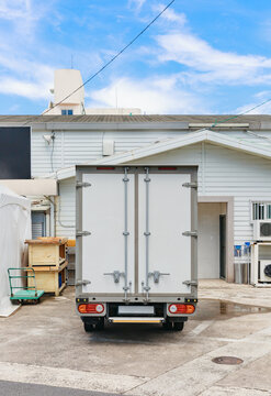 Back door of a box truck parked in front of a white building.