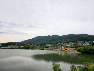A calm lake with a town in the background. The sky is cloudy and the water is still