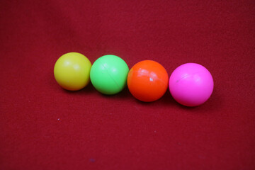 Several toy balls are pink, yellow, green and orange on a red background