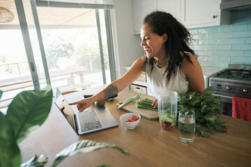 Cheerful woman cooking in kitchen and watching tutorial