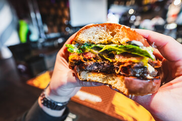 Close-up of a hand holding a half-eaten burger with lettuce and tomato, showcasing a casual dining...