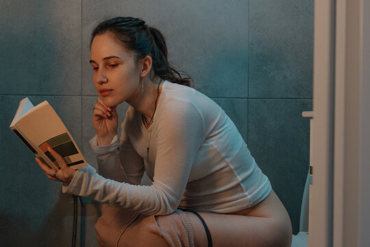 Woman reading book on toilet near dog