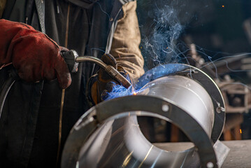Male welder wearing a protective mask is welding stainless pipe