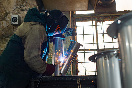 Male welder is welding stainless pipe in industrial workshop