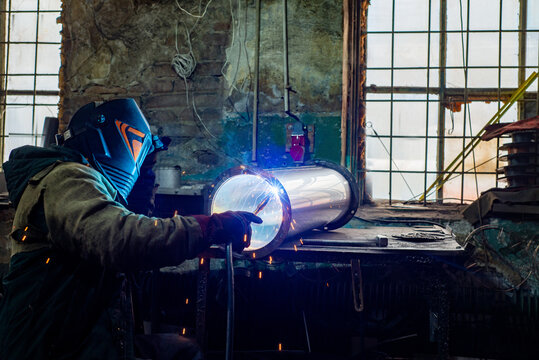 Male welder is welding stainless pipe in industrial workshop