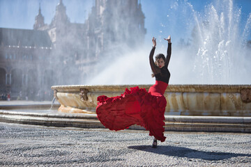 Young, beautiful, brunette woman in black shirt and red skirt, dancing flamenco in front of a...