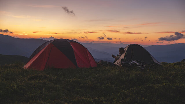 Man with bike in camping tent surfing in social media in his phone.
